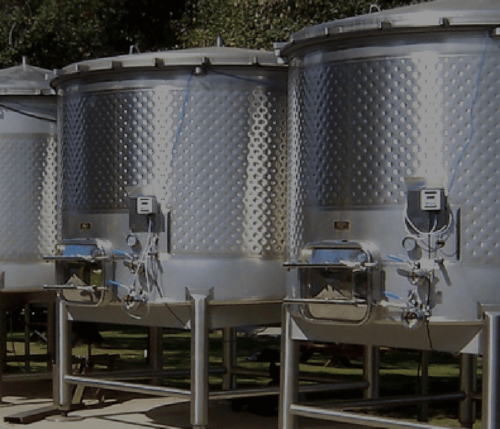 Two winery fermentation tanks outside with green trees behind.